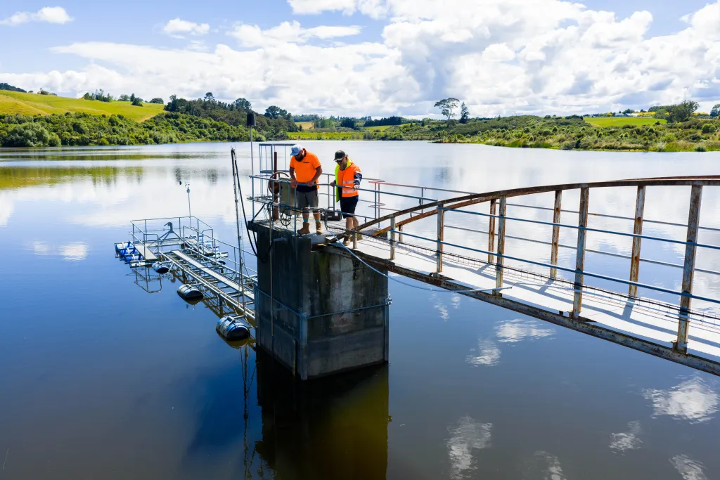 A photo of two Council water operations staff working inspecting equipment at Tūtaenui Reservoir on a sunny say.