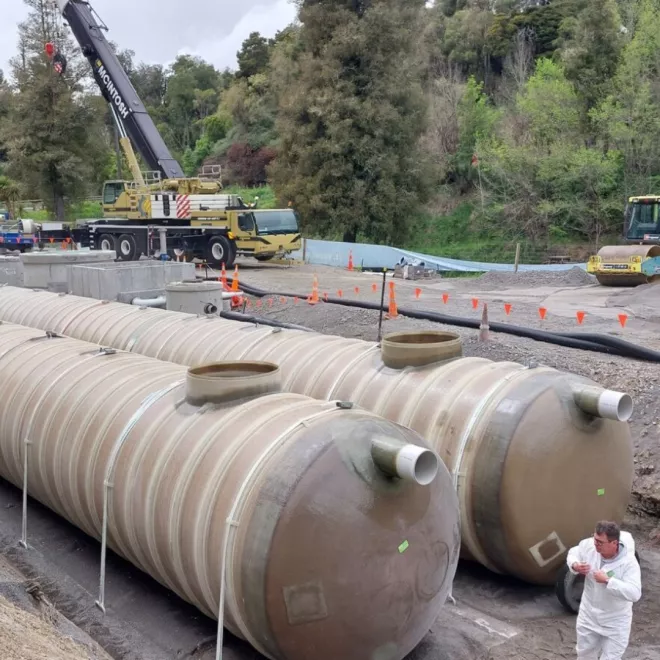 The two tanks are in place and work is happening on them to make them operational. A worker is in the foreground of the photo doing a task.