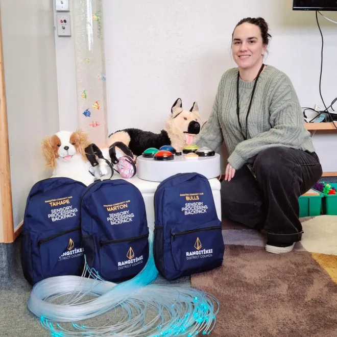 Lashana posing with the grab kit bags, with sensory play items in front of the bags.